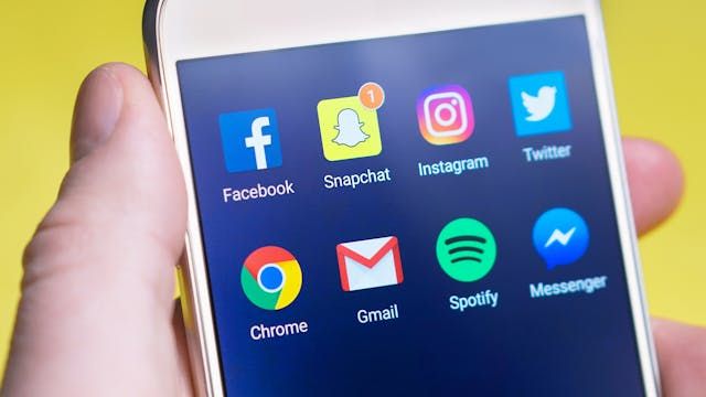 A cell phone in hand with social media apps on the screen